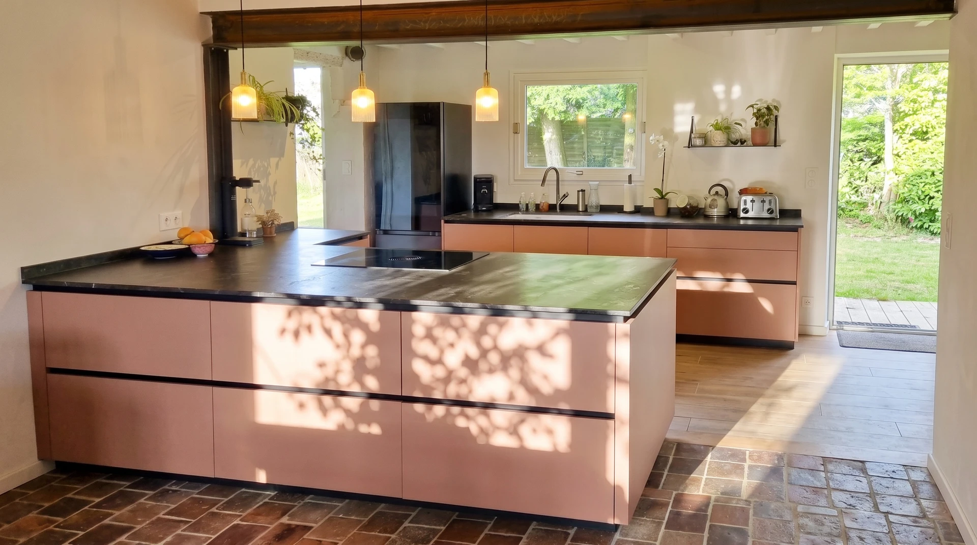 Photographie d'une cuisine moderne ouverte rénovée entièrement équipée : façades laquées blanc mat ou terracotta contemporain, plan de travail en quartz ou granit, îlot central avec plaque de cuisson intégrée, électroménagers inox encastrés (four multifonction, micro-ondes), hotte design, crédence carrelage ou effet béton, sol carrelage grand format. La pièce est lumineuse et vide de personnes, mettant en avant le savoir-faire en menuiserie et agencement. Vision frontale ou légèrement en angle pour montrer la totalité du projet rénové, incarnant le positionnement d'interlocuteur unique capable de coordonner rénovation complète et pose d'équipements haut de gamme.